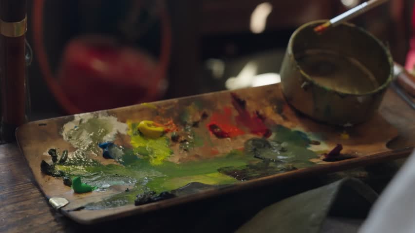 Senior artist on a wheelchair paints an oil painting on canvas in a studio