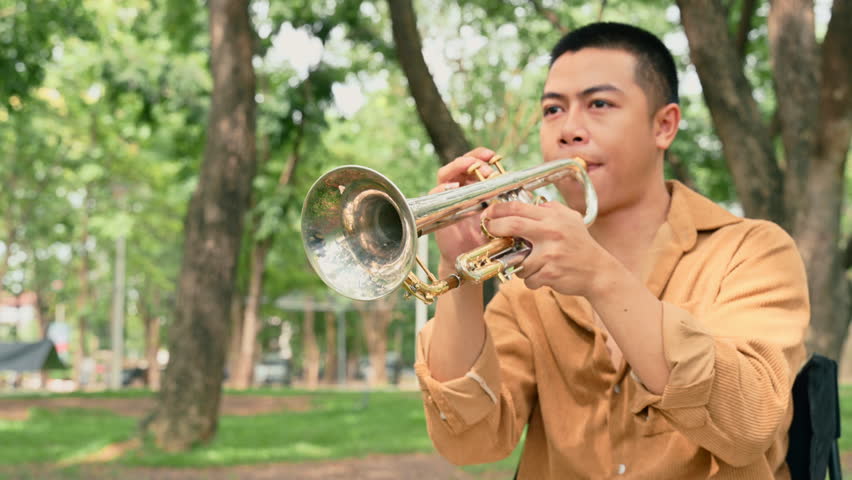 Young man playing trumpet outdoors in a peaceful green park