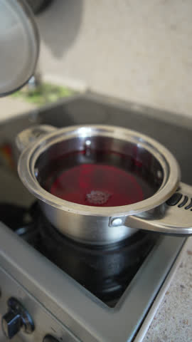 Cooking Pot Stove Hand lifts lid during cooking on electric hob in kitchen daytime