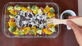 Vegetables including broccoli, yellow bell peppers, tomatoes, and onions arranged in a glass dish, being brushed with herb marinade before baking, healthy and colorful meal prep - Powered by Shutterstock - Get 15% off with code: PIKWIZARD15