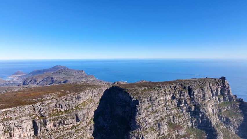 Spectacular aerial pan down shot of Table Mountain Cape Town South Africa revealing the iconic flat-topped mountain plateau dramatic cliffs and the Atlantic Ocean under a clear blue sky