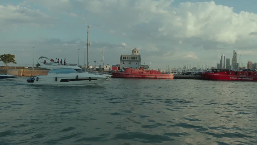 Luxury yacht cruising past the Chicago Fire Department boats at sunset near the marina, with the city skyline in the background.
