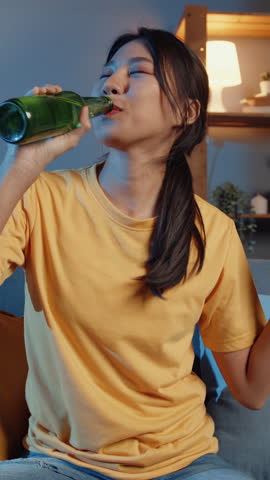 Vertical Screen : Happy young asian woman looking at camera enjoy night party event online with friends toast drink beer via video call online in living room at home. Social distancing concept.