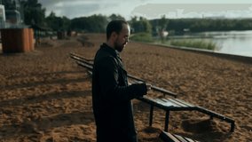 A pensive man smokes a cigarette alone near a sandy beach, dressed in black, immersed in a heavy emotional moment of regret, sadness, and personal struggle. - Powered by Shutterstock - Get 15% off with code: PIKWIZARD15