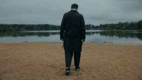 Young male wearing dark coat walks alone on sandy lake shore, overcast clouds above create a vibe of loneliness, sadness and inner reflection. - Powered by Shutterstock - Get 15% off with code: PIKWIZARD15