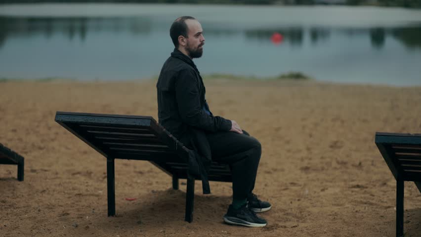 Middle-aged man alone at the beach, dressed in black, silently dealing with emotional weight. Peaceful yet heavy moment, full of solitude and quiet sorrow.