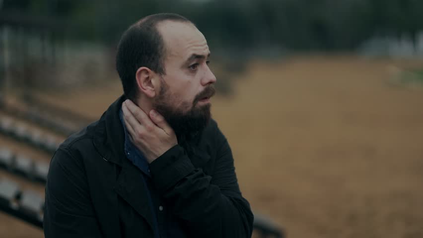 Balding man with a beard looks down in silence, seemingly consumed by his thoughts. The somber tone suggests loneliness, pain, or emotional fatigue.