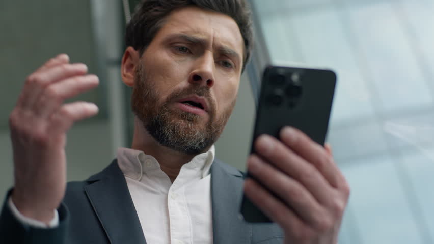 Close up unhappy frustrated Caucasian middle-aged business man reading bad news with mobile phone online failure upset in office worried stressed businessman male manager employer smartphone problem