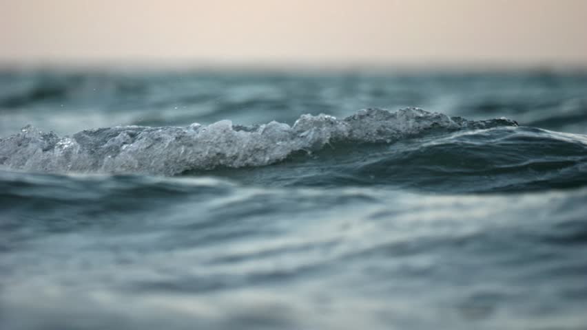 Slow motion recording of ocean swell at sunset with compressed wave layers from a telephoto perspective.