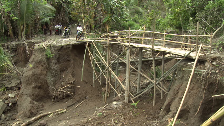 Motorbikes cross dangerously unstable makeshift bridge made of bamboo in rural