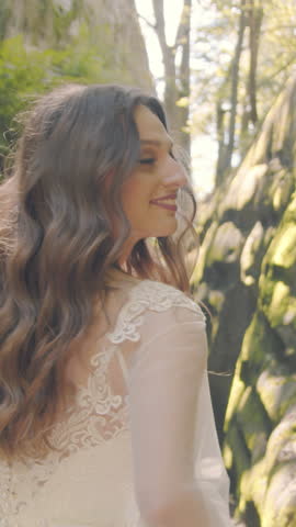Bride runs between cliffs under golden sun. Her white dress glows in the backlight, and joyful energy shines from her face as she smiles straight to the camera.