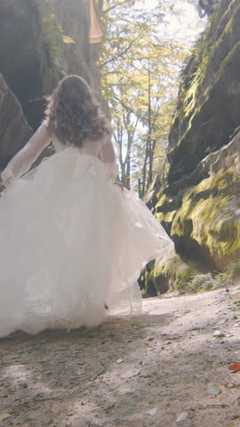 Bride runs between coastal rocks, smiling into the lens. Backlit by the sun, her dress glows with golden flares as she enjoys the joy of the wedding day.