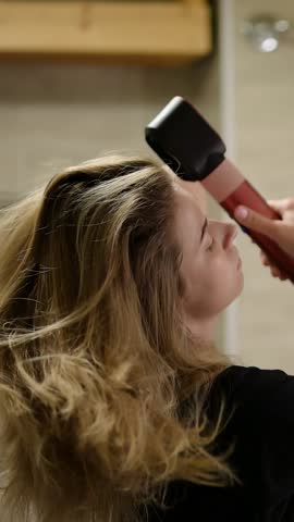 Woman styling hair with heated tool in modern bathroom setting during morning routine
