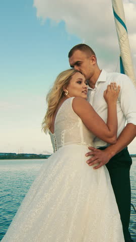 Bride rests her head on groom s chest aboard a sailing yacht. He gently kisses her as they look into each other s eyes, surrounded by sea and sunlight.