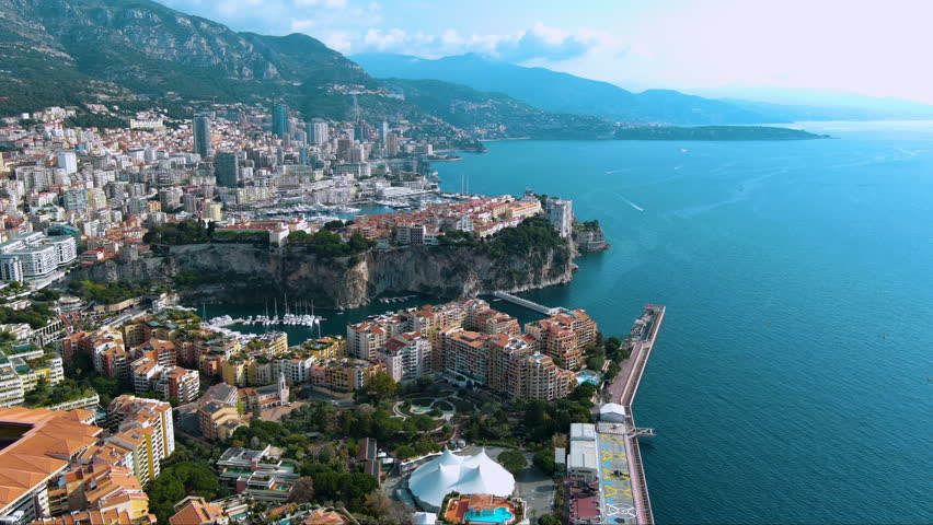 Luxury drone panorama of Monaco’s dramatic cliff‑top Old Town, super‑yacht harbours of Port Hercule and Fontvieille, terracotta apartments and sparkling Mediterranean framed by Alpine foothills.
