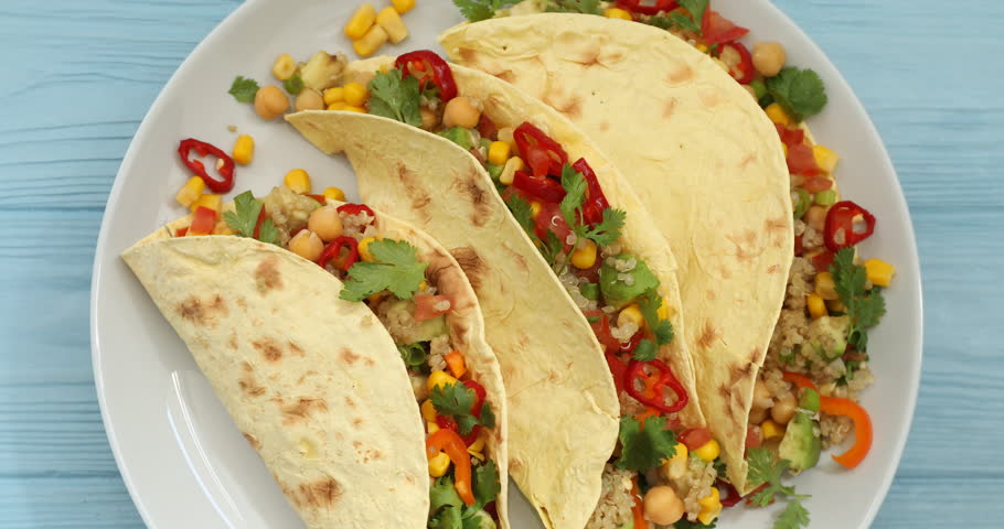 Tasty vegetarian tacos with chickpeas, corn and quinoa spinning on light blue wooden table, top view