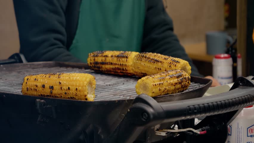 At the bustling Christmas market, vendors prepare baked corn, creating a tempting aroma that fills the air, blending sweet and salty flavors this holiday season.