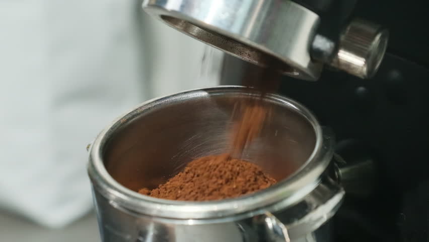 Coffee powder coming out of professional coffee machine fills metal portafilter. Presentation of part of making coffee slow motion