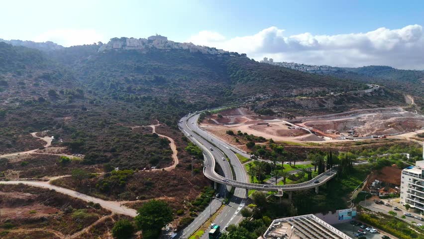 Aerial drone view of Haifa, Israel, showing highway interchanges, urban buildings, and cityscape infrastructure from above.

