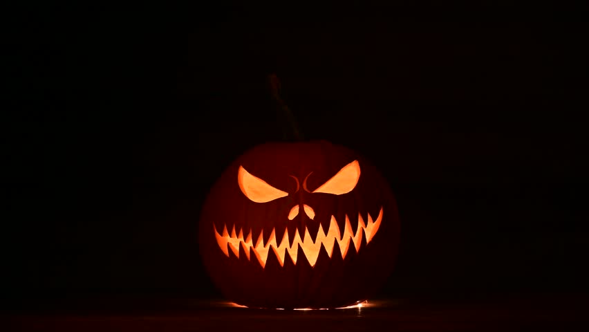 Pumpkin lantern glows with pulsing light in dark Halloween scene. Creepy carved face shines in night mood with seasonal mystery and fall decor