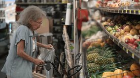 An elderly woman carefully selects fruits while grocery shopping with the assistance of her walker in a supermarket filled with fresh produce. - Powered by Shutterstock - Get 15% off with code: PIKWIZARD15