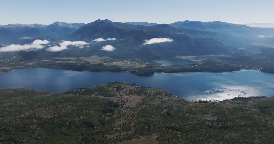 Lake Ñorquinco nestled amidst rolling, forested hills under a clear sky. Distant mountain ranges of Los Andes, Patagonia, Argentina