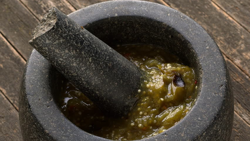 Homemade roasted tomatillo salsa with dried and toasted chilies de arbol in molcajete. Typical mexican dip. Rustic wooden table.
