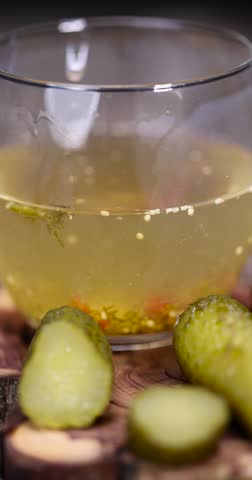 cucumbers marinade and pickled next to a glass, poured pickle marinade with spices and whole crispy cucumbers on a board