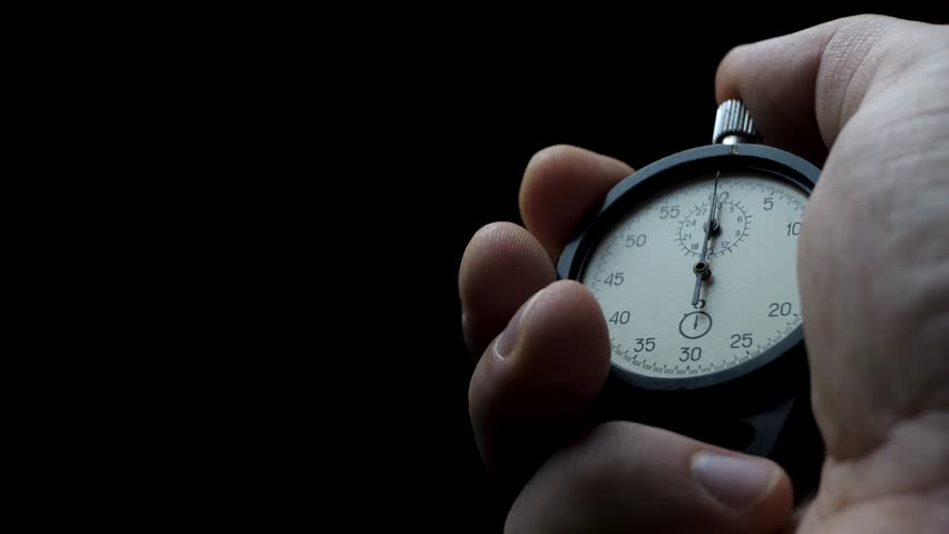 Male hand holds stopwatch and starts countdown. Second hand begins first tick. Concept of time control. Focus on precision and discipline. Dark background enhances intensity