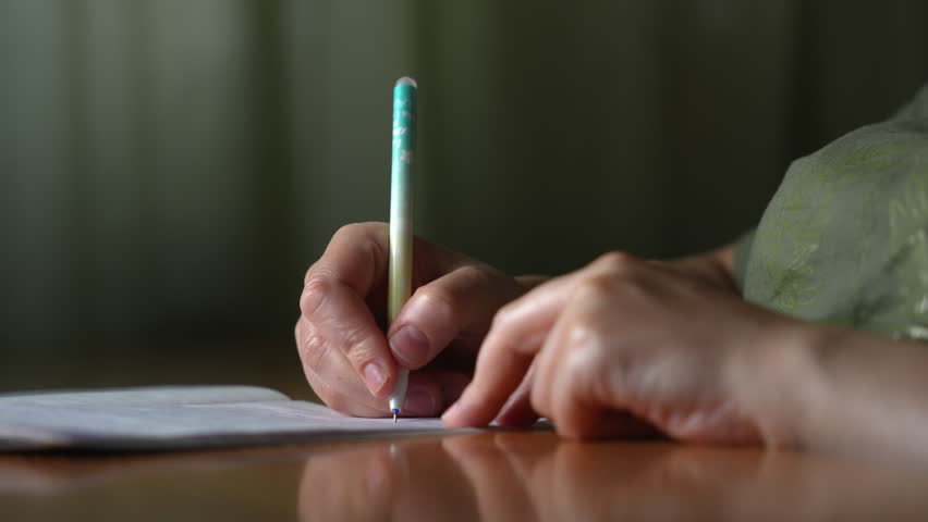 Close-up of female hands writing in a notebook with a pen, studying or taking notes in a calm and focused environment.