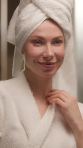 Beautiful happy girl Caucasian woman bathrobe towel massaging neck cream skincare smiling cheerful female young gorgeous model look mirror touching soft skin enjoying shower beauty routine lotion bath