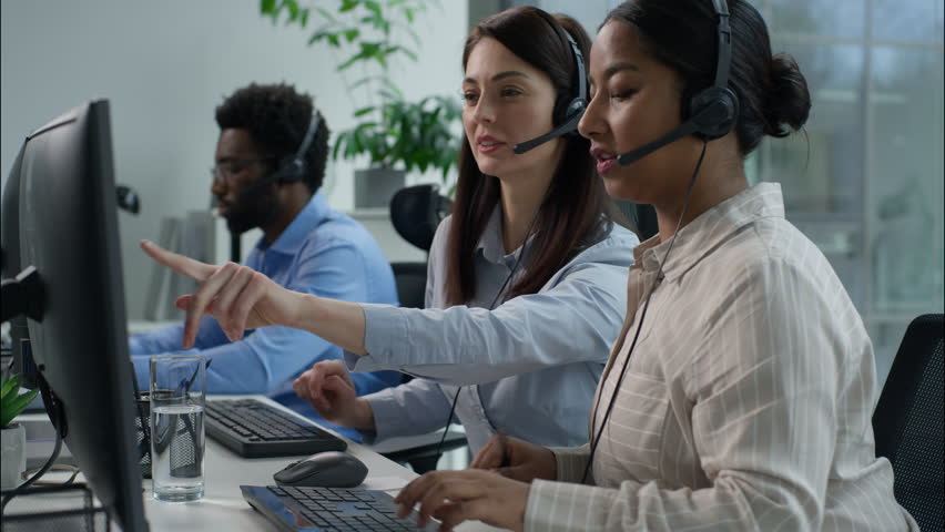Cooperation Caucasian operator helping call center coworker Indian worker talking helpline women African men in headset typing computer writing notes callcenter support online trading sales at office - Powered by Shutterstock - Get 15% off with code: PIKWIZARD15