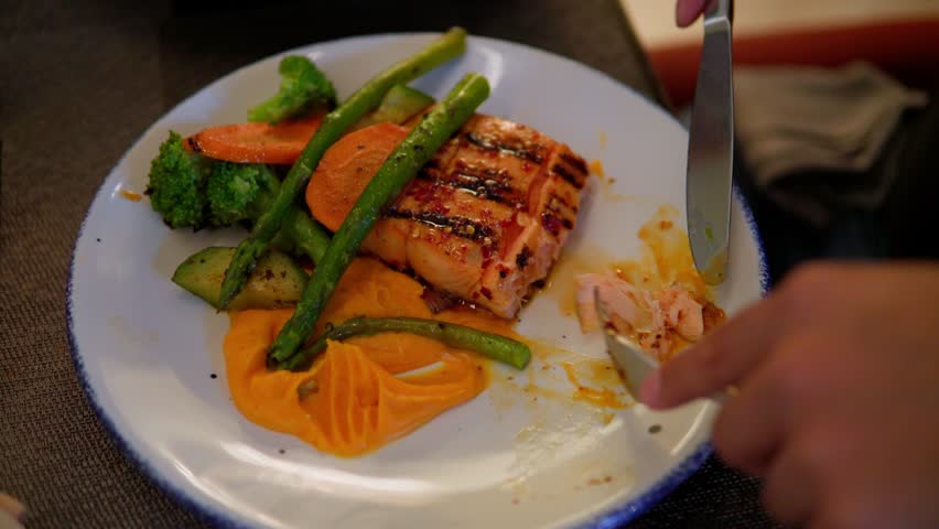 Grilled salmon fillet being savored with a side of steamed vegetables and mashed sweet potatoes
