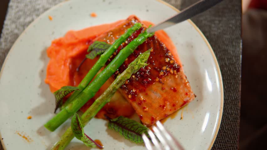 Customer cutting grilled salmon steak with sweet potato puree and asparagus
