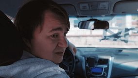 A man with short brown hair sitting in the driver seat of a car looks over his shoulder toward the back seat, with a steering wheel and dashboard partially visible - Powered by Shutterstock - Get 15% off with code: PIKWIZARD15
