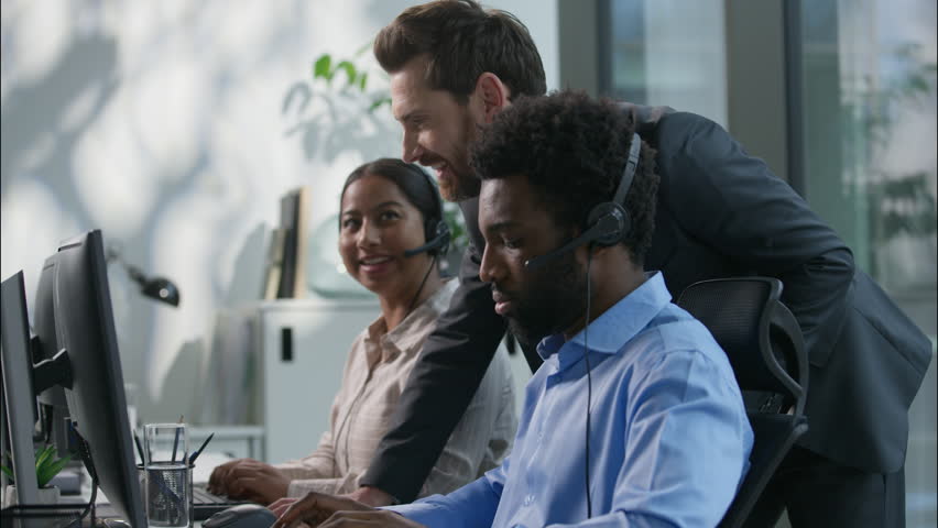 Multiethnic callcenter smiling Caucasian boss explain pointing pc monitor Indian woman employee office teamwork business call center customer support training African man headset helpline hotline desk - Powered by Shutterstock - Get 15% off with code: PIKWIZARD15