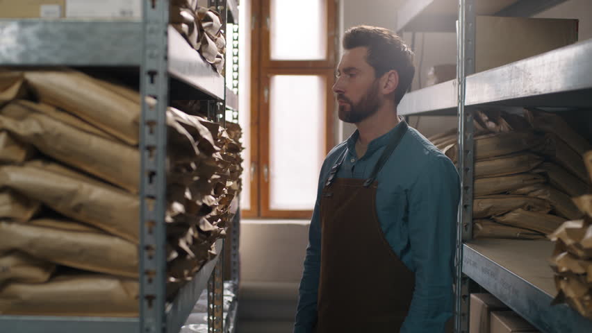 Focused concentrated Caucasian man male coffee factory worker searching beverage grains sort warehouse shelf storage aroma selection quality barista looking for caffeine packaging roasted grain indoor