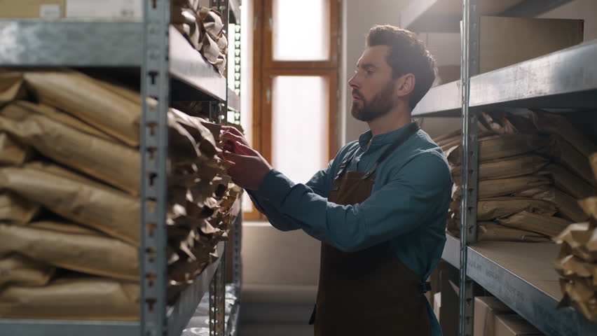Focused concentrated Caucasian man male coffee factory worker searching beverage grains sort warehouse shelf storage aroma selection quality barista looking for caffeine packaging roasted grain indoor