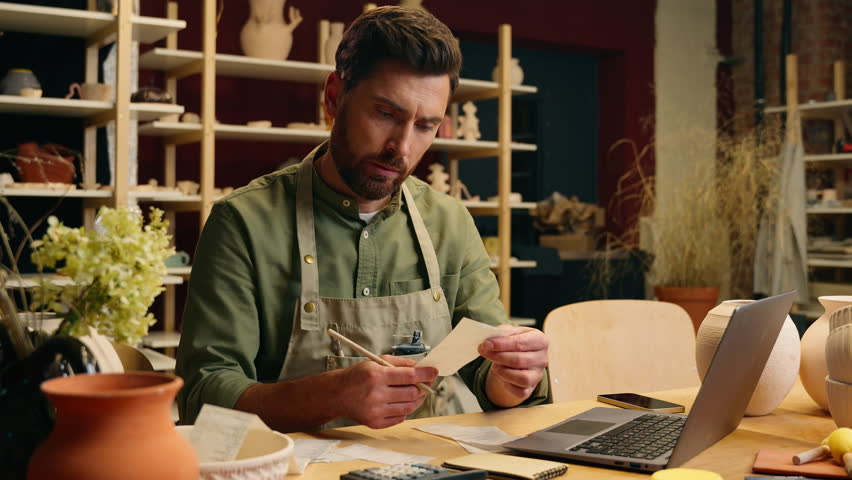 Frustrated despair Caucasian man guy businessman male small business owner potter crock working laptop calculating finance debt look receipt holding head gesture frustration bankruptcy inside workshop