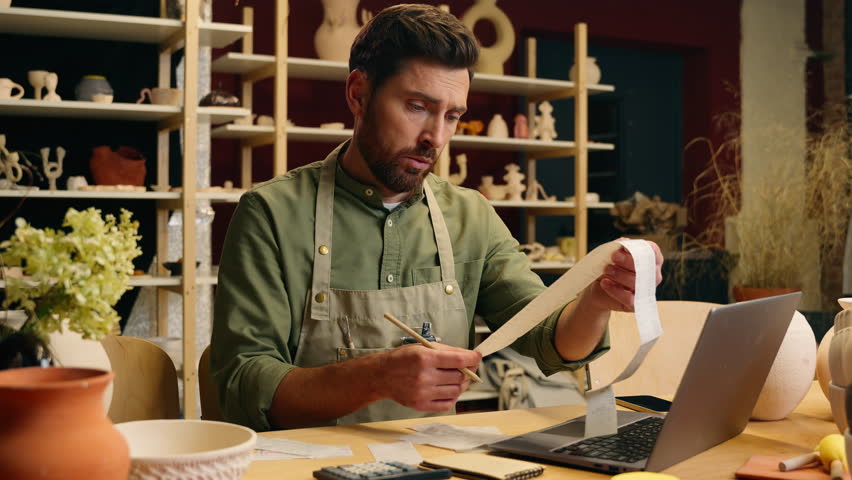 Frustrated despair Caucasian man guy businessman male small business owner potter crock working laptop calculating finance debt look receipt holding head gesture frustration bankruptcy inside workshop