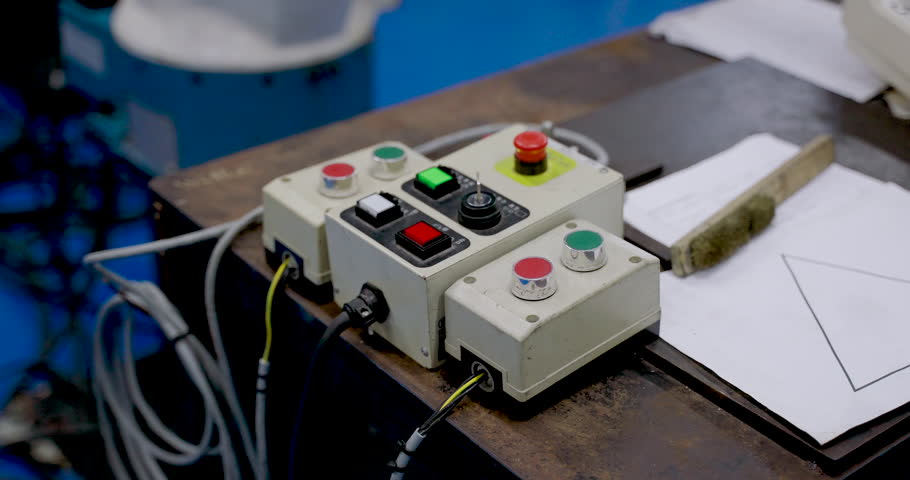 Close up of control panel with emergency stop buttons and cables placed on workbench during robotic training session in industrial automation lab for factory safety and system handling