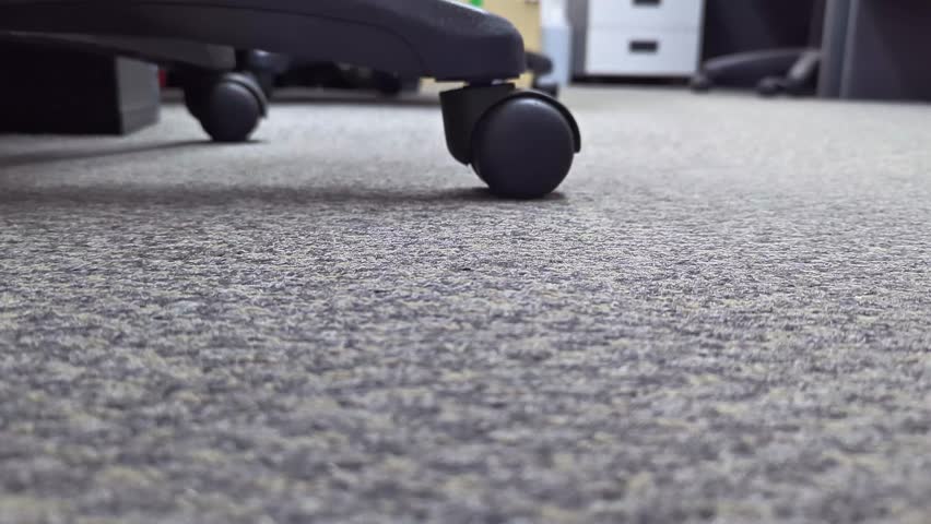Close-up of an office chair wheel rolling on carpet flooring. Concept of business routines, workspace movement, office environment, or ergonomic furniture.