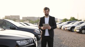 A car salesman invites the viewer to look at the available cars, holding a tablet while smiling at the camera. - Powered by Shutterstock - Get 15% off with code: PIKWIZARD15
