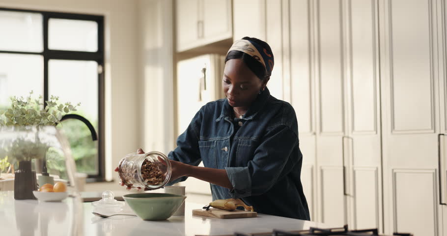 Pour cereal, breakfast and black woman with nutrition, healthy diet and wellness in kitchen. Home, morning and prepare food in bowl with hungry person for vegan meal, organic or natural with fiber