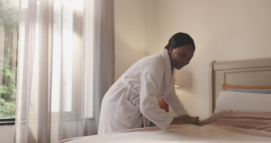 Smile, black woman and making bed in hotel room for morning routine, maintenance and getting ready. Tourist, hospitality and cleaning in bedroom of resort for travel, vacation and holiday with robe