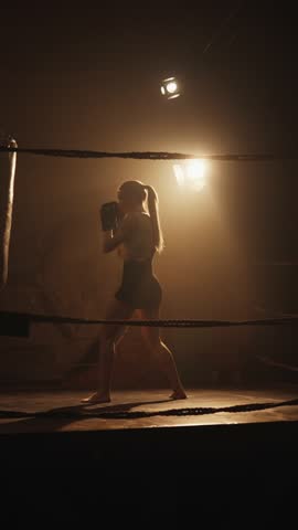 Beautiful woman boxing alone in darkness, lady striking punch bag on ring. Active sport workout for stay healthy and slender, fitness and physical exercise for keep fit, silhouette of slender woman