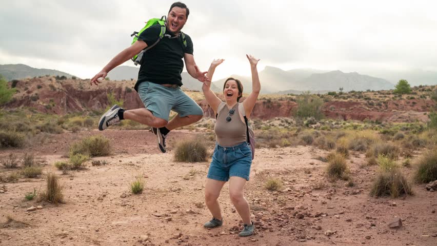 Creative animation made from still photos showing a happy couple jumping in excitement while hiking in a scenic mountainous desert landscape. Ideal for nature, adventure, or travel-themed content. 4K