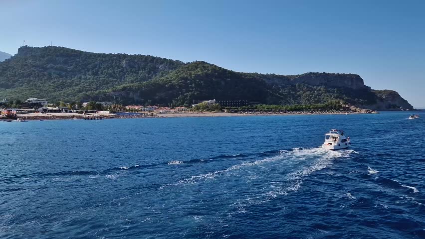Seaside view to Kiris resort near Kemer, Turkey, with boats cruising on the deep blue Mediterranean Sea. Majestic Taurus mountain on the coastline background