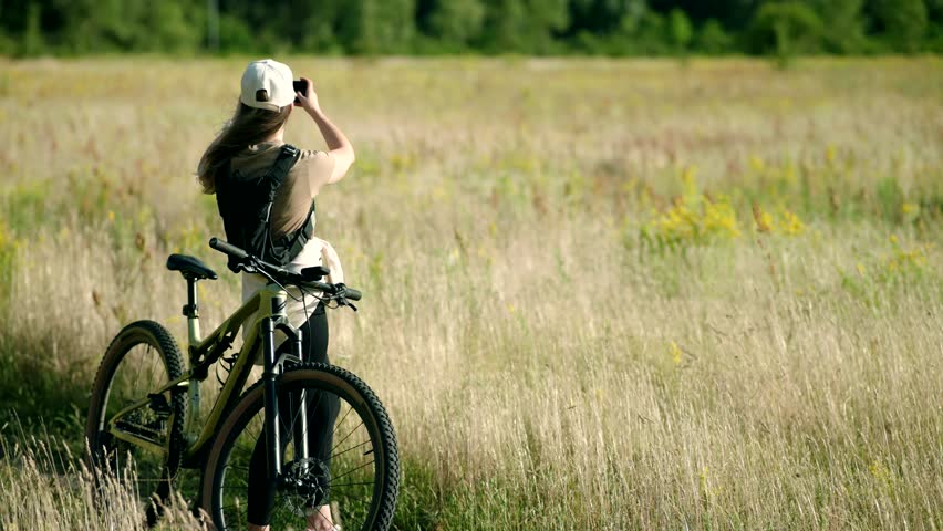 Cyclist takes photo on smartphone while riding mountain bike. Captures scenic beauty of nature on cycling adventure.Active lifestyle, travel, leisure eco-tourism nature exploration in rural landscapes