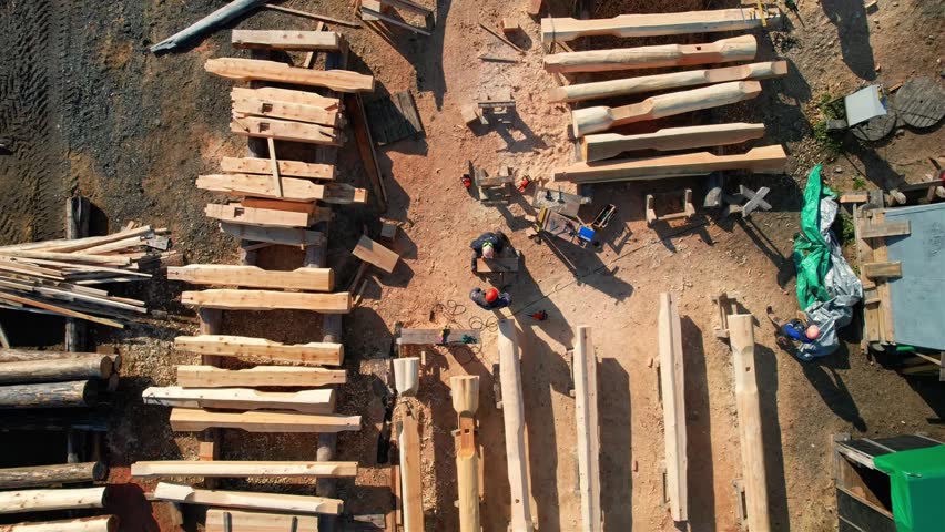 Aerial view of wooden house frame construction captured. Building processing with workers maneuvering logs.